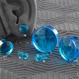 May include: A set of blue glass ear gauges in various sizes, including 1/2 inch, 6 gauge, 4 gauge, 1 inch, and 7/8 inch. The gauges are made of clear glass with a blue tint.