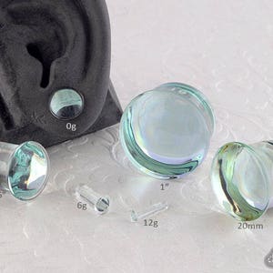 May include: A set of six glass ear gauges in various sizes, ranging from 9/16 inch to 1 inch. The gauges are clear with a light blue iridescent sheen.