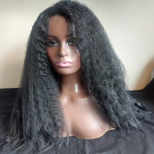Peut inclure: Perruque noire avec de longs cheveux texturés, présentée sur une tête de mannequin. La perruque présente une ligne de cheveux d'apparence naturelle et une couleur charbon de bois foncé. Les cheveux ont une texture frisée, donnant du volume et un style unique.