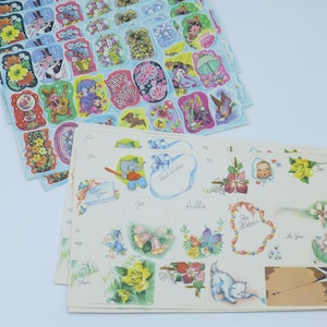 Op de afbeelding: Vellen vintage stickers met diverse ontwerpen, waaronder bloemen, stripfiguren en verjaardagswensen. Sommige stickers hebben tekst zoals "Happy Birthday" en "For Baby". De stickers zijn in verschillende vormen en kleuren.