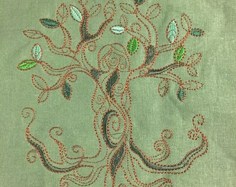 May include: Embroidered design of a tree with a brown trunk and green leaves on a green fabric background.