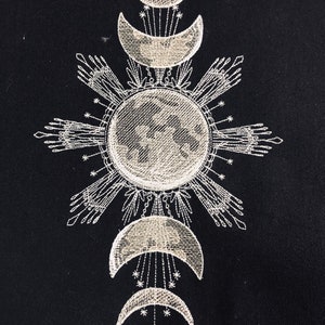 May include: Embroidered design on black fabric featuring a stylized sun with rays and a crescent moon with stars. The design is repeated in a vertical pattern with three moons and a sun.