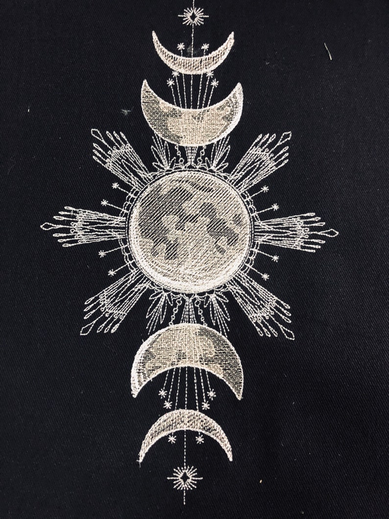 May include: Embroidered design on black fabric featuring a stylized sun with rays and a crescent moon with stars. The design is repeated in a vertical pattern with three moons and a sun.