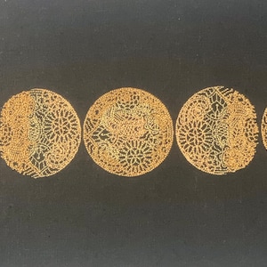 May include: Embroidered design of seven crescent moons in gold thread on a black fabric background. The moons are arranged in a row, with the full moon in the center.