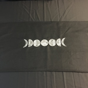 May include: Black fabric table runner with a white embroidered design of a crescent moon and six full moons.