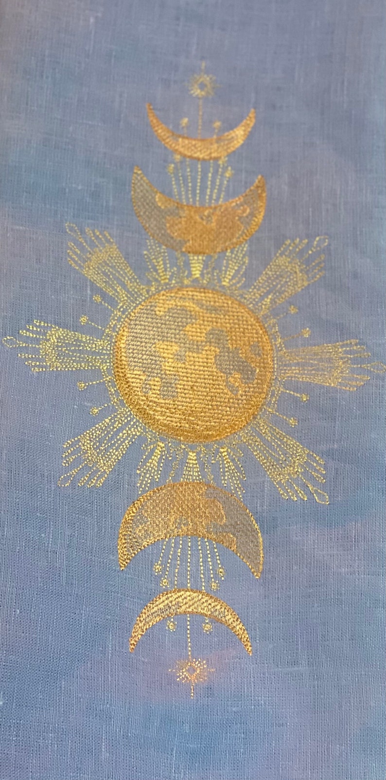 May include: A gold embroidered design on a light blue fabric featuring a sun with rays and a crescent moon with stars.
