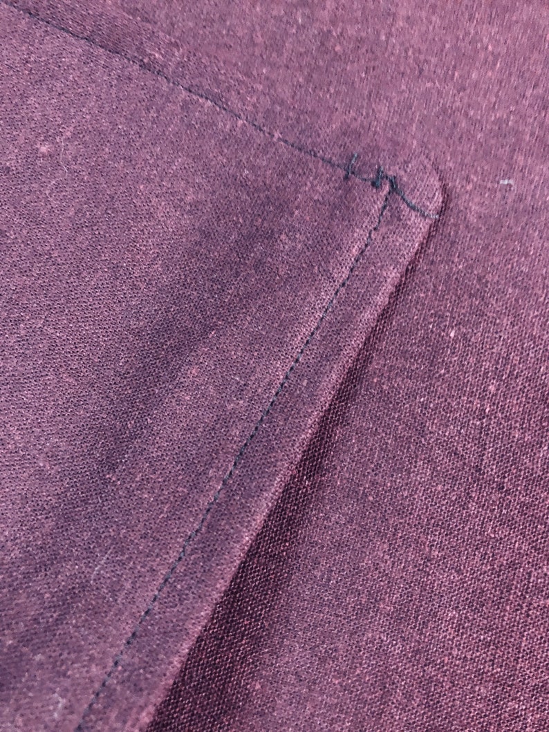 May include: Close-up of a dark purple fabric with a black stitched seam. The fabric has a textured, woven appearance.