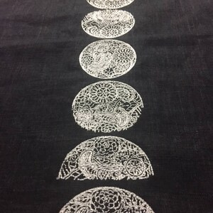 May include: A black fabric with a white embroidered design of eight different phases of the moon.
