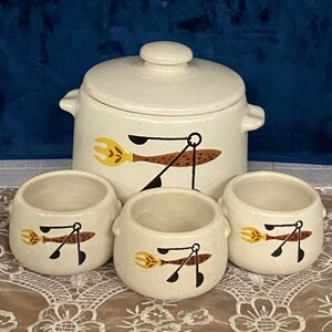 May include: A set of four white ceramic bowls with brown, black, and yellow designs. The bowls are arranged in a circle with a larger white ceramic bowl with a lid in the center. The larger bowl also has a brown, black, and yellow design.