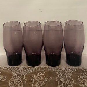 May include: Set of four purple glass tumblers. The glasses are clear with a purple tint and have a rounded bottom.