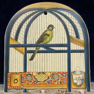 May include: A decorative arched wall plaque featuring a painted illustration of a bird inside a blue cage. The base displays a vibrant orange panel with yellow and purple floral patterns, a small circular symbol, and a blue and white landscape vessel.