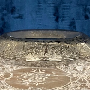 May include: A clear glass bowl with a decorative etched floral pattern. The bowl is round and has a wide rim.