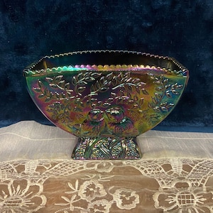May include: Iridescent glass bowl with a square shape and scalloped rim. The bowl features a raised floral and bird design. The colors shift from green to purple and gold. The bowl sits on a pedestal base.