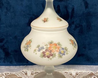 May include: A white frosted glass candy dish with a floral design. The dish has a round base and a domed lid. The flowers are painted in shades of orange, pink, purple, and blue.