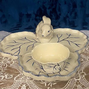May include: A three-part serving dish with a bunny figurine. The dish is leaf-shaped with blue veins and a blue scalloped edge. The center bowl and bunny are off-white.