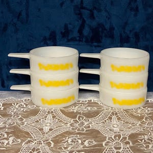 May include: Set of four white ceramic mixing bowls with yellow bands. The bowls are stacked on top of each other.