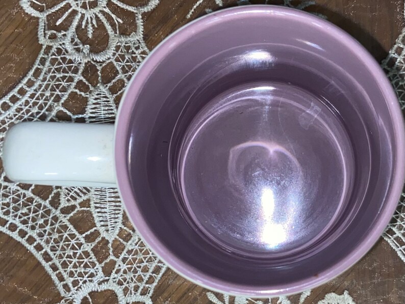 Op de afbeelding: Een keramische mok van bovenaf bekeken, met een gladde, glanzende lavendelkleurige binnenkant en een witte buitenkant. De mok heeft een stevig, afgerond wit handvat aan de linkerkant en een eenvoudig, functioneel ontwerp.