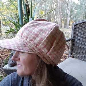 May include: A plaid newsboy cap in cream and red. The cap has a rounded crown and a short, stiff brim. The fabric has a classic plaid pattern. The cap is designed to be worn outdoors.