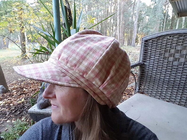 May include: A plaid newsboy cap in cream and red. The cap has a rounded crown and a short, stiff brim. The fabric has a classic plaid pattern. The cap is designed to be worn outdoors.