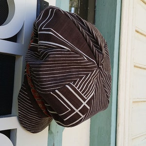 May include: A brown hat with a geometric pattern of white lines and shapes. The hat is hanging on a white door with a black screen. The hat has a rounded shape and a brim that is not visible.