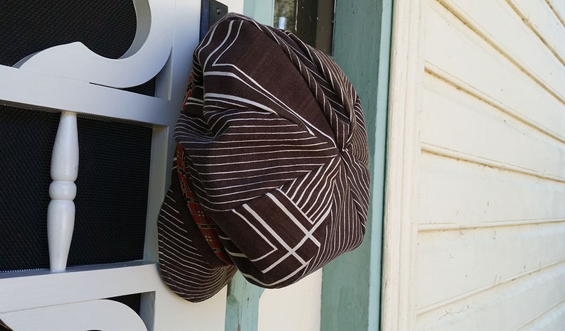 May include: A brown hat with a geometric pattern of white lines and shapes. The hat is hanging on a white door with a black screen. The hat has a rounded shape and a brim that is not visible.