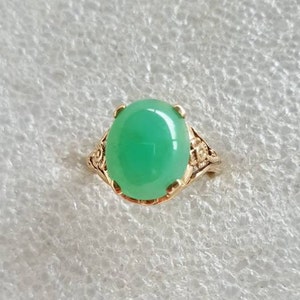 May include: A green gemstone ring with a gold setting. The ring has a delicate floral design.