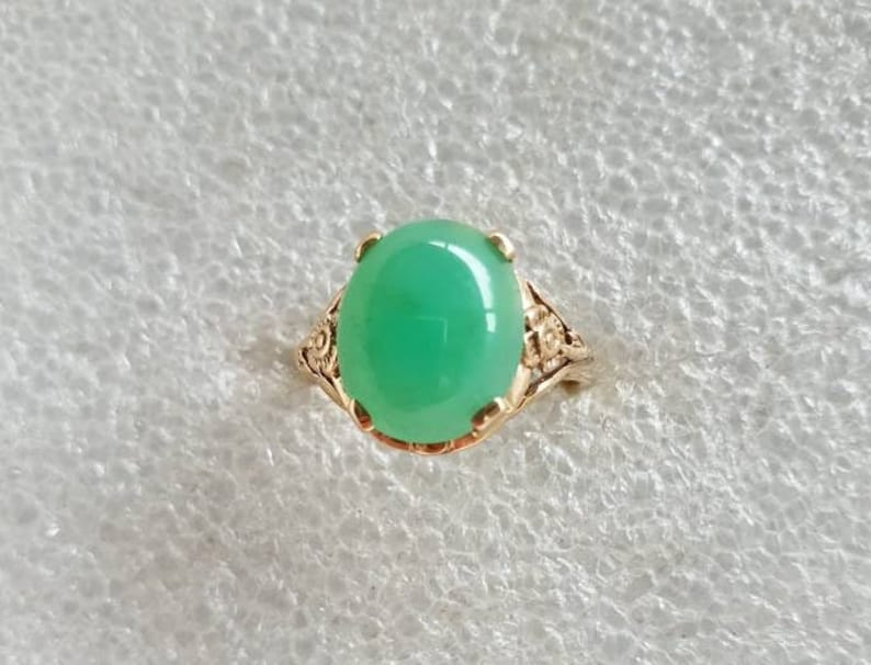 May include: A green gemstone ring with a gold setting. The ring has a delicate floral design.