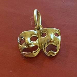 May include: A gold-colored pendant charm featuring two theatrical masks, one smiling and one frowning.
