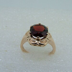 May include: A rose gold ring with a red gemstone set in a floral design.