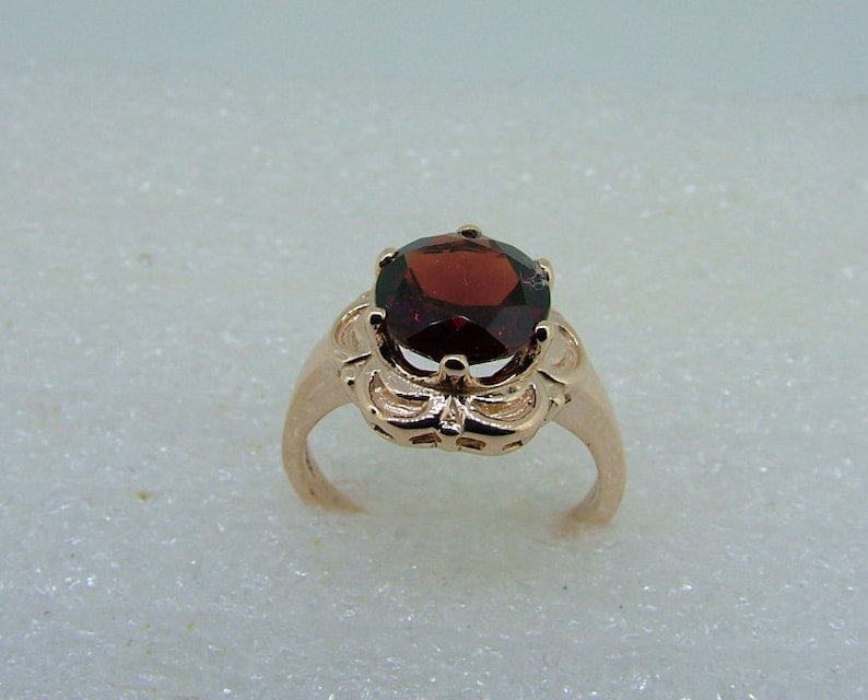 May include: A rose gold ring with a red gemstone set in a floral design.