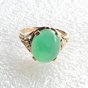 May include: A gold ring with a large, oval-shaped green gemstone set in a delicate floral design.