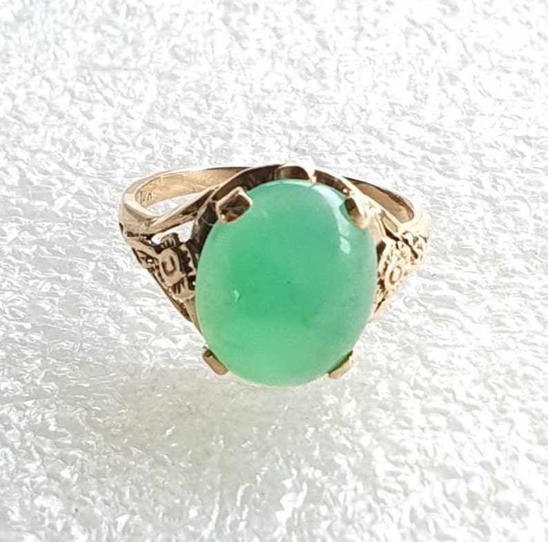 May include: A gold ring with a large, oval-shaped green gemstone set in a delicate floral design.