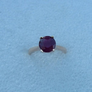 May include: A ring with a large, round, dark red ruby gemstone set in a silver band.