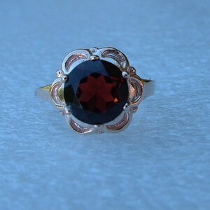 May include: A silver ring with a dark red gemstone set in a floral design.