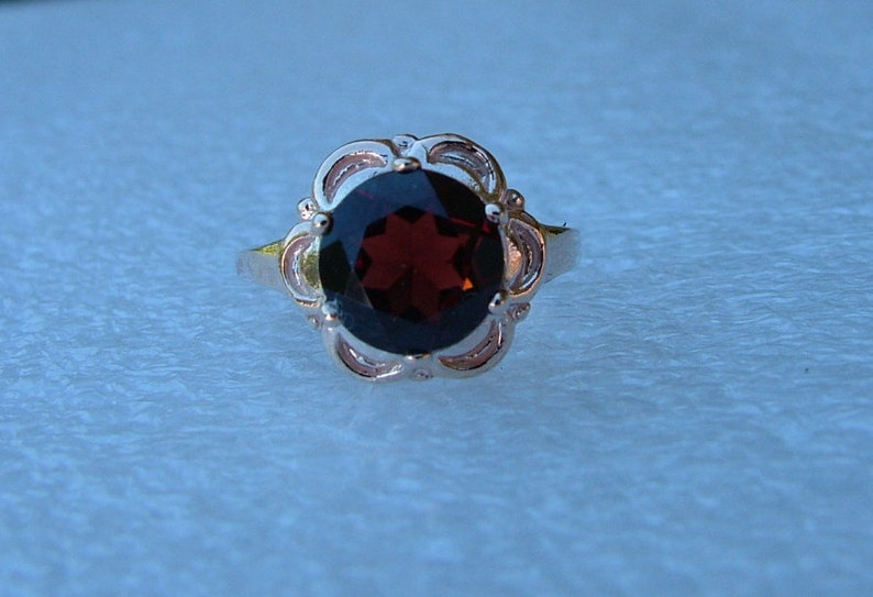 May include: A silver ring with a dark red gemstone set in a floral design.