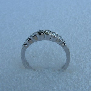May include: A silver band ring with a row of small, clear round stones set in the band.