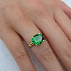 Puede incluir: Un anillo de oro con una gran piedra preciosa de color verde esmeralda de forma ovalada.