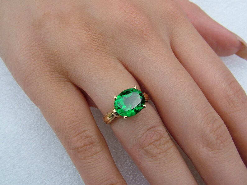 Puede incluir: Un anillo de oro con una gran piedra preciosa de color verde esmeralda de forma ovalada.