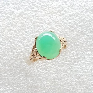 May include: A green gemstone ring with a gold setting. The ring features a delicate floral design.