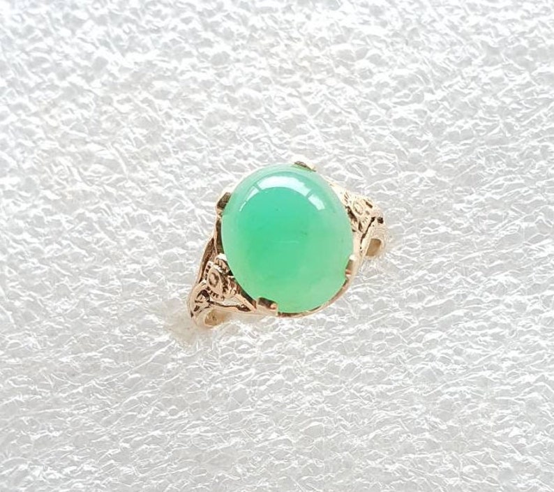 May include: A green gemstone ring with a gold setting. The ring features a delicate floral design.
