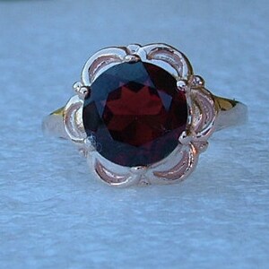 May include: A silver ring with a large, oval-shaped, dark red garnet gemstone set in a delicate, floral-inspired design.