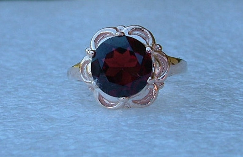 May include: A silver ring with a large, oval-shaped, dark red garnet gemstone set in a delicate, floral-inspired design.