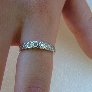May include: A silver band ring with a row of round, clear gemstones.