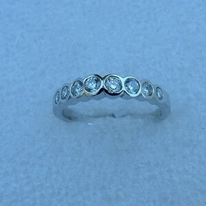 May include: A silver band ring with a row of round, clear gemstones.