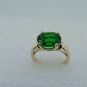 Puede incluir: Un anillo de oro con una gran piedra preciosa verde de forma ovalada.