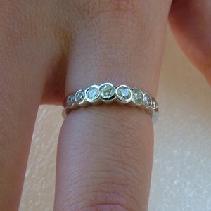 May include: A silver band ring with a row of round, clear gemstones.