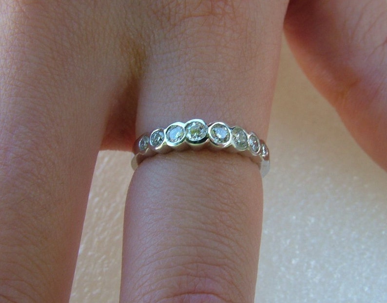 May include: A silver band ring with a row of round, clear gemstones.