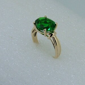 Puede incluir: Un anillo de oro con una gran piedra preciosa verde de forma ovalada. El anillo tiene un dise&ntilde;o simple y elegante.
