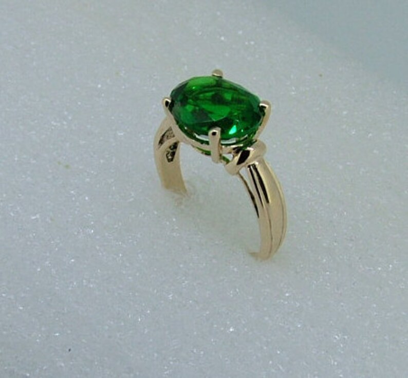 Puede incluir: Un anillo de oro con una gran piedra preciosa verde de forma ovalada. El anillo tiene un dise&ntilde;o simple y elegante.