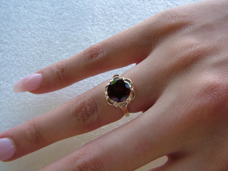May include: A gold ring with a dark red gemstone set in a delicate floral design.